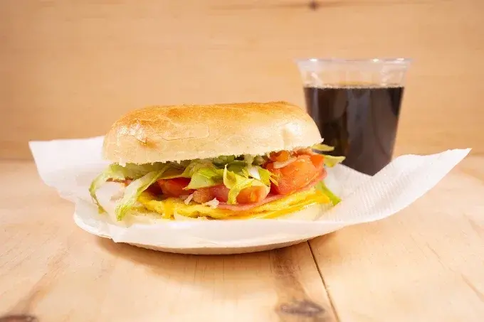 A breakfast sandwich with egg, tomato and lettuce on a fresh bun, served with a coffee