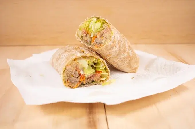 A grilled wrap sliced in half showing chicken, lettuce and carrot, served on parchment