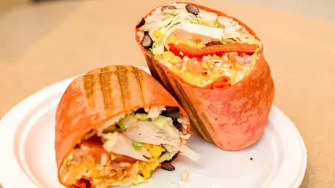 A sun-dried tomato wrap cut in half, filled with chicken, rice, black beans, corn and lettuce