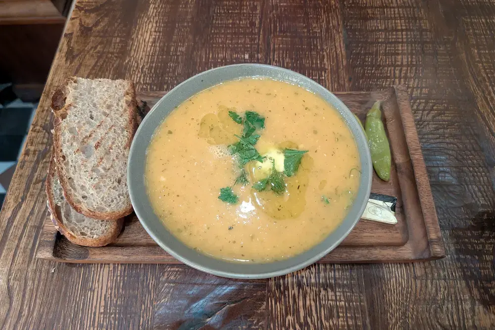 A bowl of creamy golden lentil soup topped with fresh herbs and olive oil, served on a wooden board with slices of sourdough